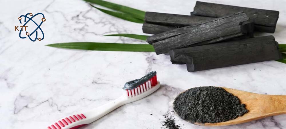 پودر سیاه کربن فعال داخل قاشق چوبی، تکه های ذغال و خمیردندان سیاه روی مسواک